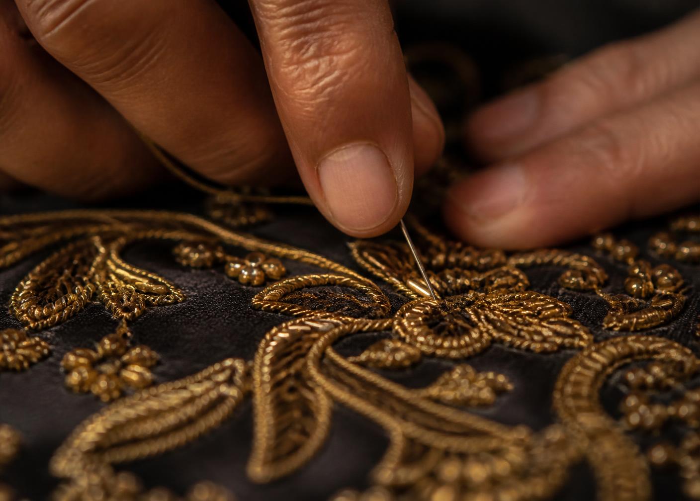 Hands working metallic gold thread embroidery onto dark silk