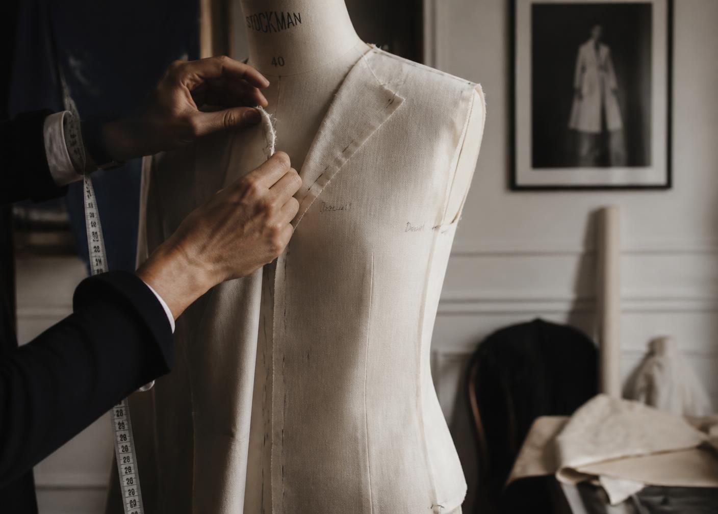 Hands pinning a canvas toile onto a tailor's dress form